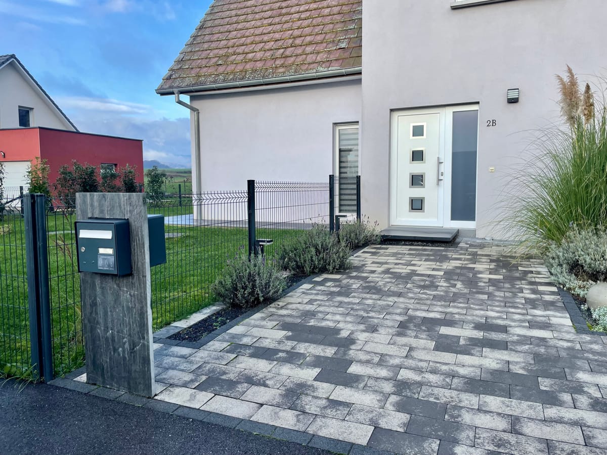 Allée pavée menant à l'entrée d'une maison, massifs et boîte aux lettres