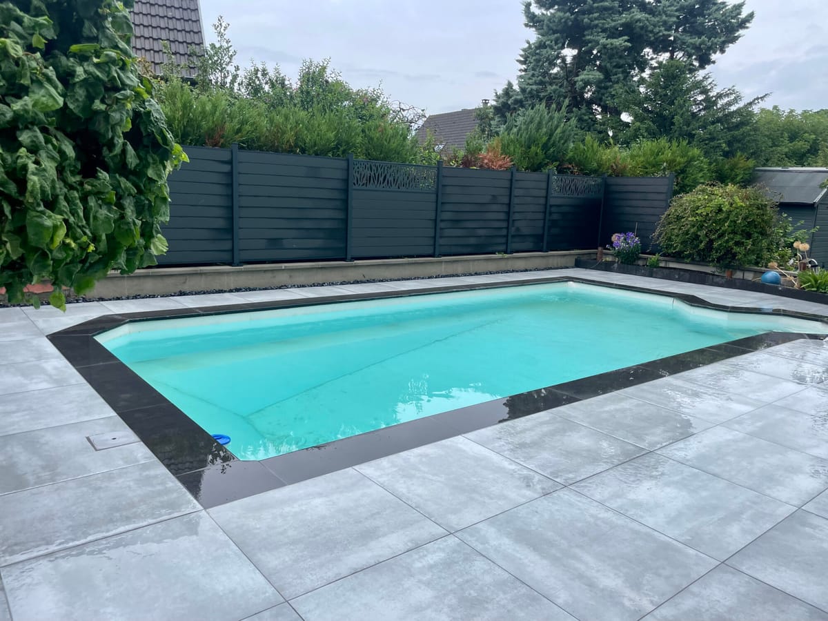 Piscine d'angle avec plage en dalles grand format et haie de thuyas