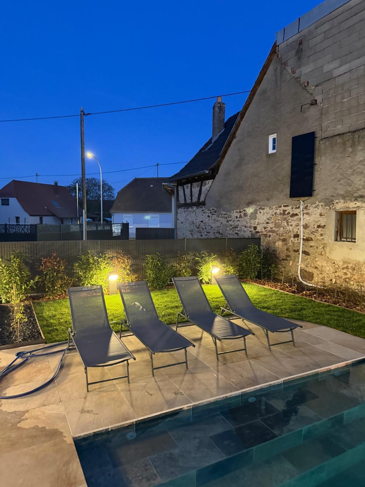 Piscine éclairée à la tombée de la nuit avec transats et éclairage extérieur intégré