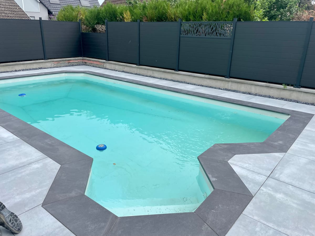 Piscine de forme libre entourée d'une plage en dalles et d'une clôture occultante