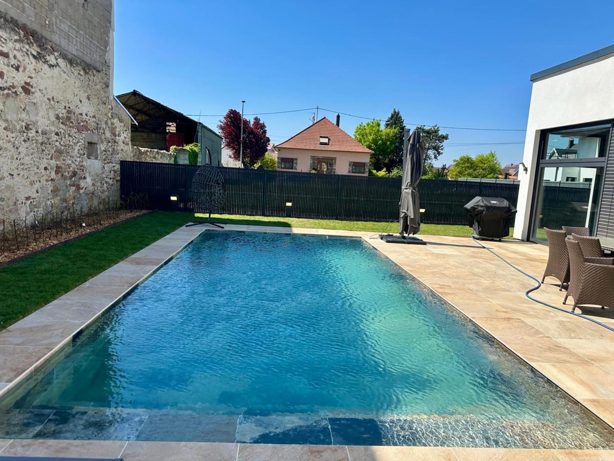 Piscine dans un jardin clos, mur de clôture sombre et pelouse en périphérie