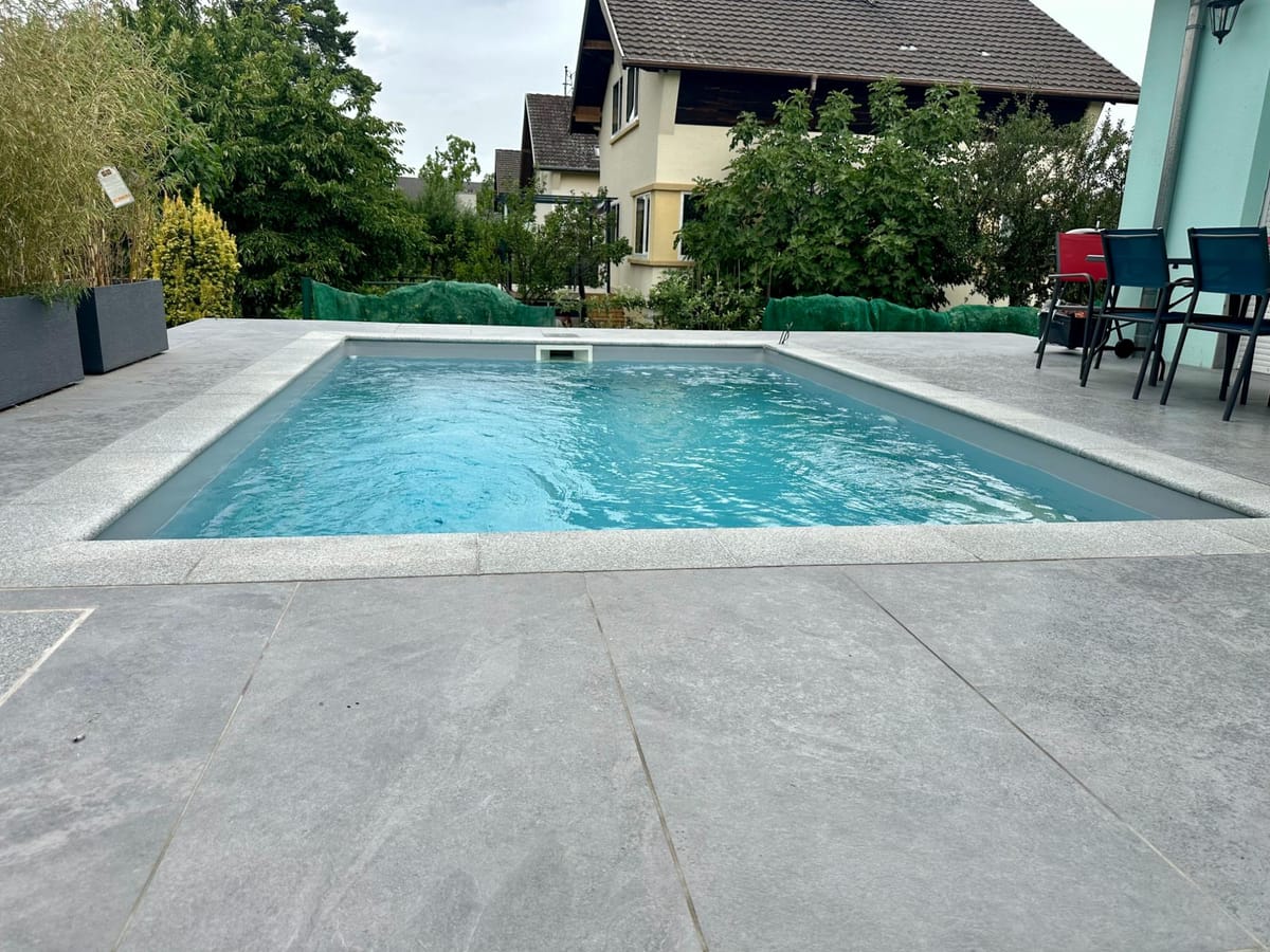 Piscine à liner gris avec plage en béton désactivé et bordure végétalisée