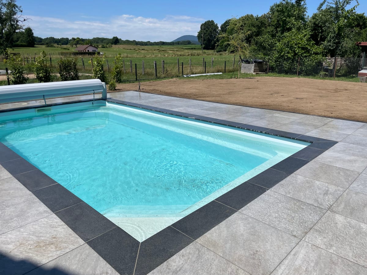 Piscine aux margelles sombres contrastant avec une plage en pierre claire