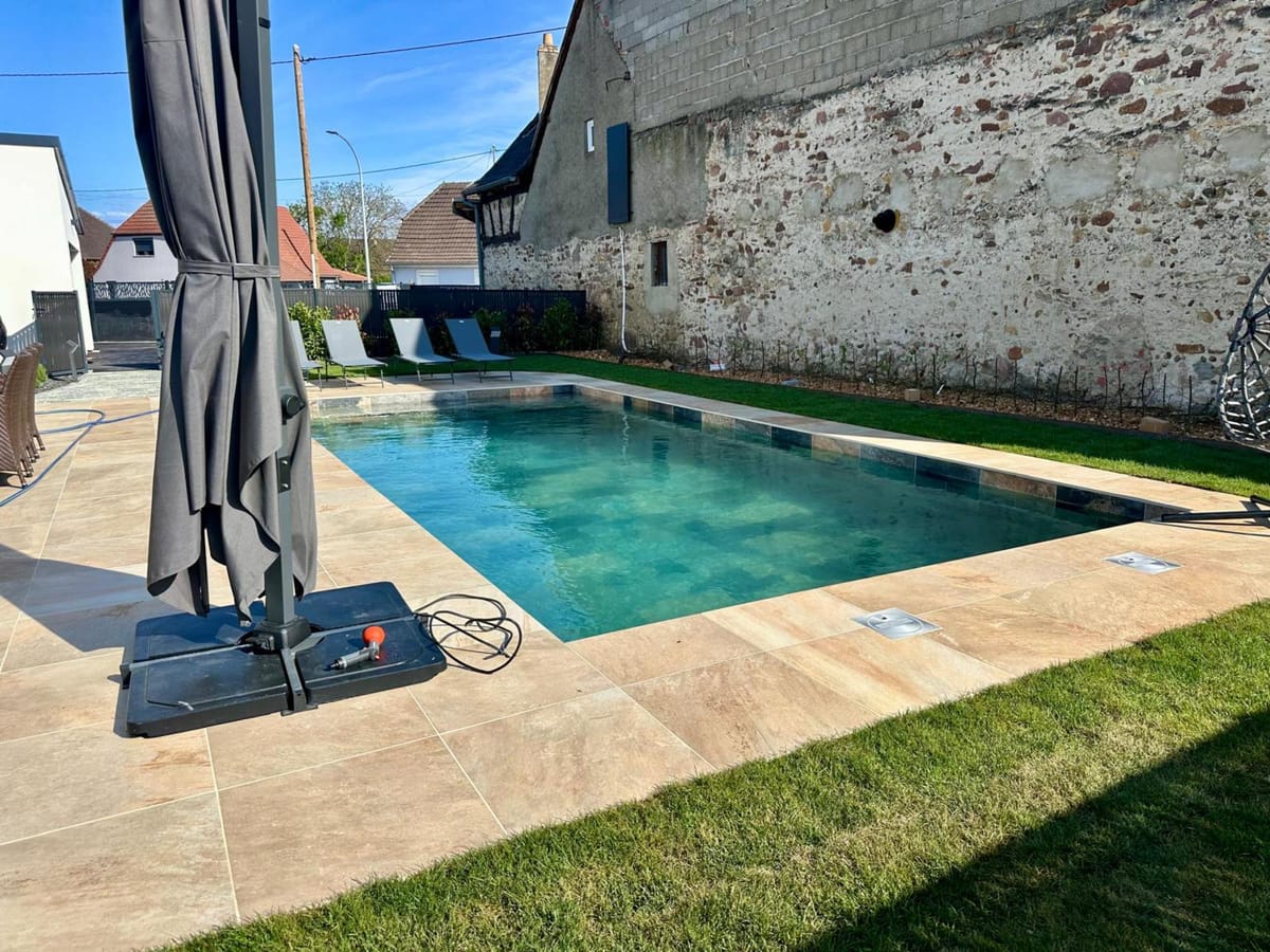 Piscine adossée à un mur en pierre ancienne à Magstatt-le-Haut, plage en travertin