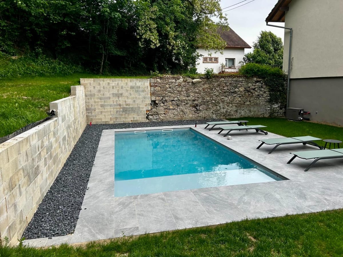 Piscine avec muret en pierre naturelle, bande de galets et transats