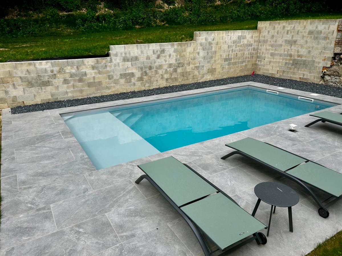 Piscine avec plage en travertin adossée à un mur en pierre ancienne, réalisée par Art Design