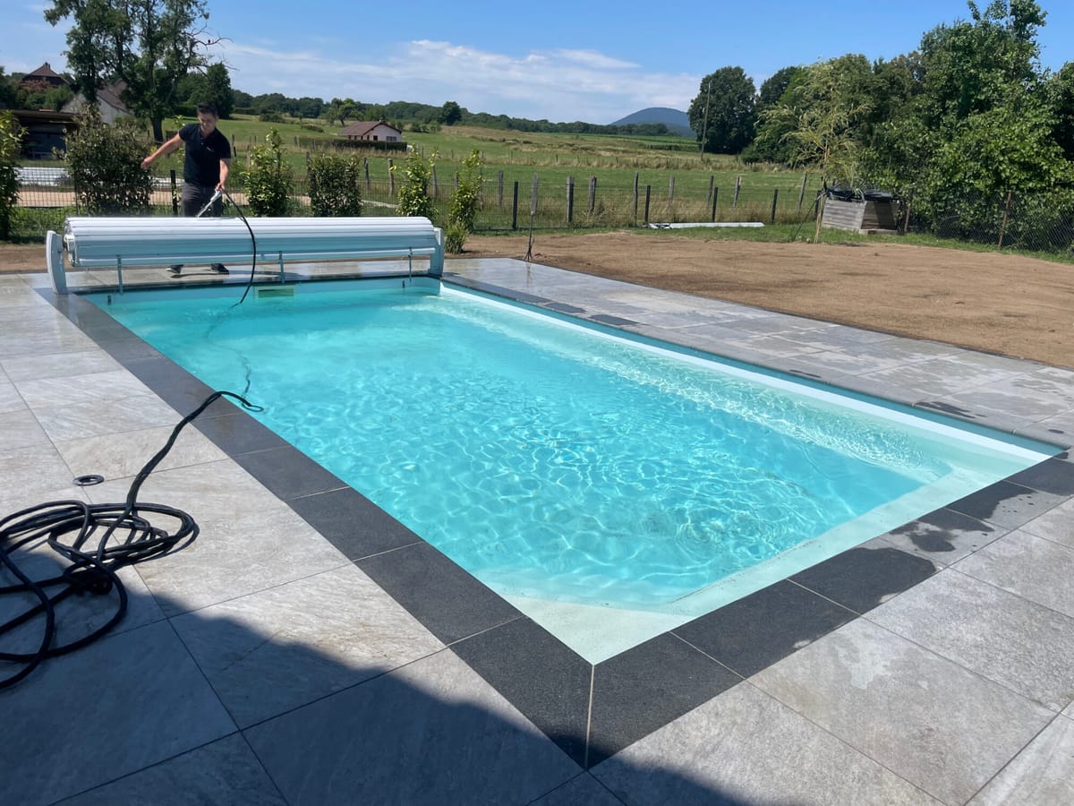 Piscine équipée d'un volet roulant, plage en dalles et vue sur la campagne